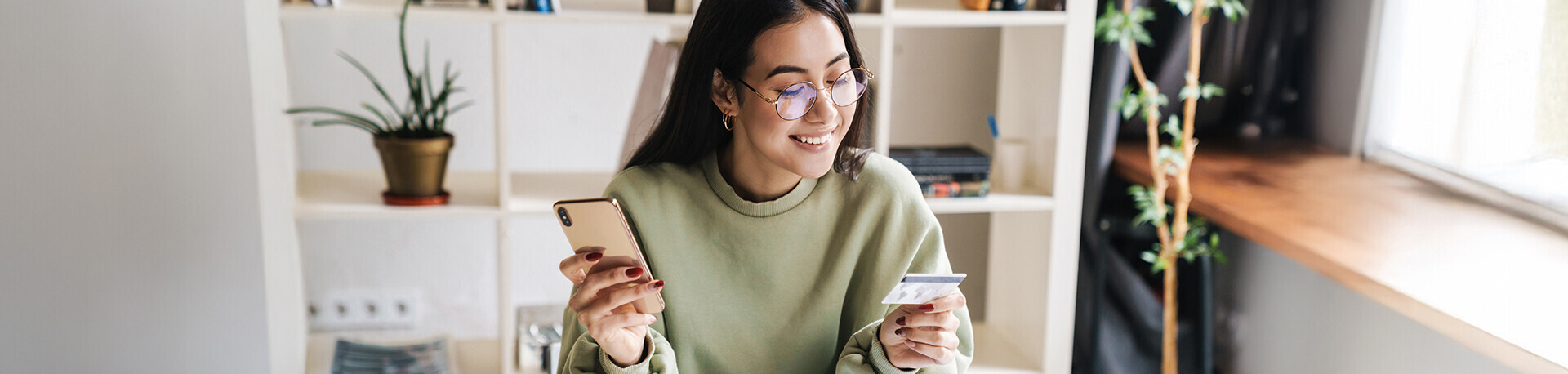 Lächelnde junge Frau mit Handy und Kreditkarte in der Hand