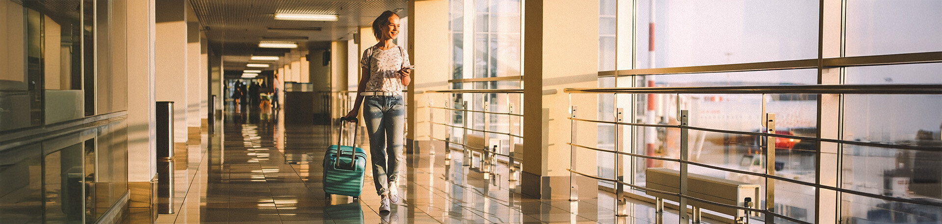 Junge Frau lachend alleine am Flughafen mit Koffer
