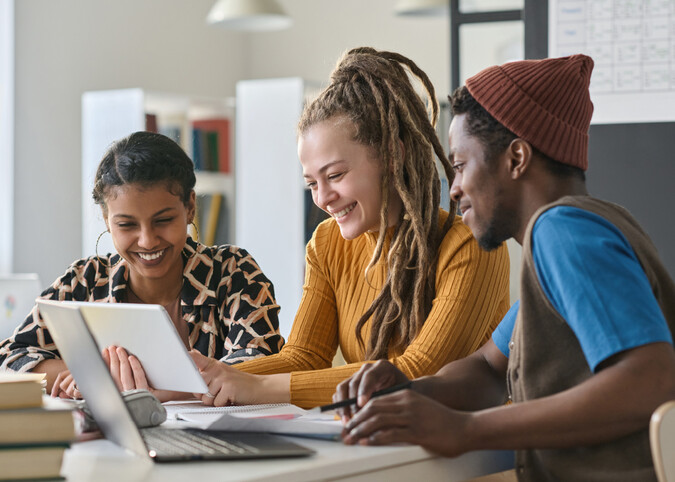 Drei junge Menschen schauen zufrieden in einen Laptop
