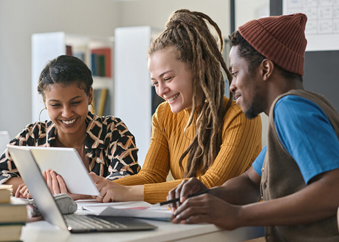 Drei Student*innen über dem Laptop gebeugt