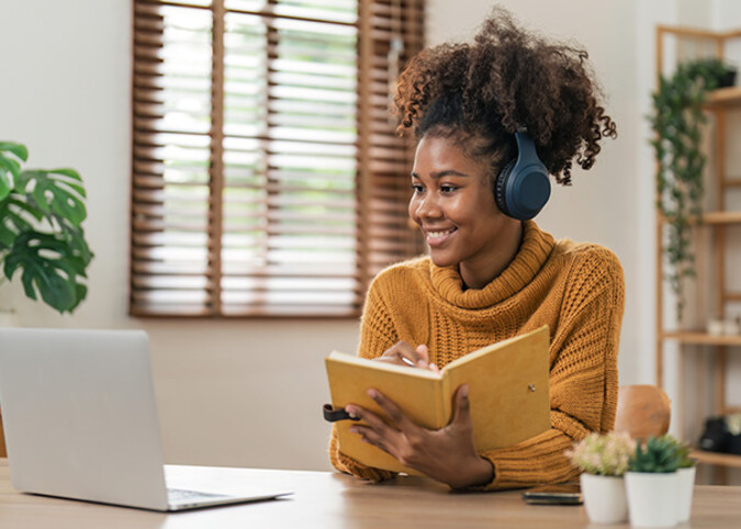 Glückliche Frau mit Buch in der Hand vor ihrem Laptop