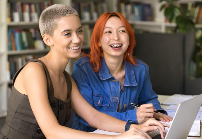 Zwei lachende Studentinnen in Bibliothek