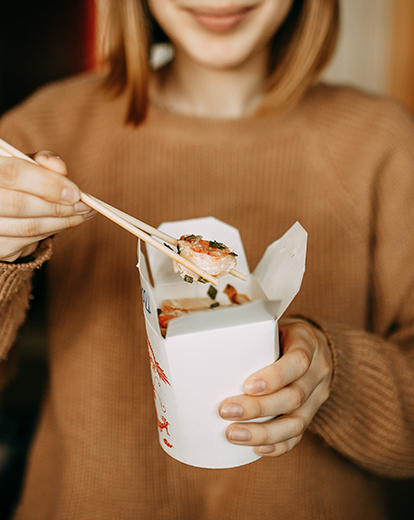 Mensch isst mit Stäbchen aus Papierbox