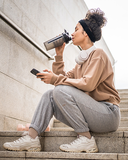 Frau sitzt auf Treppe und nimmt Schluck aus einem Shaker