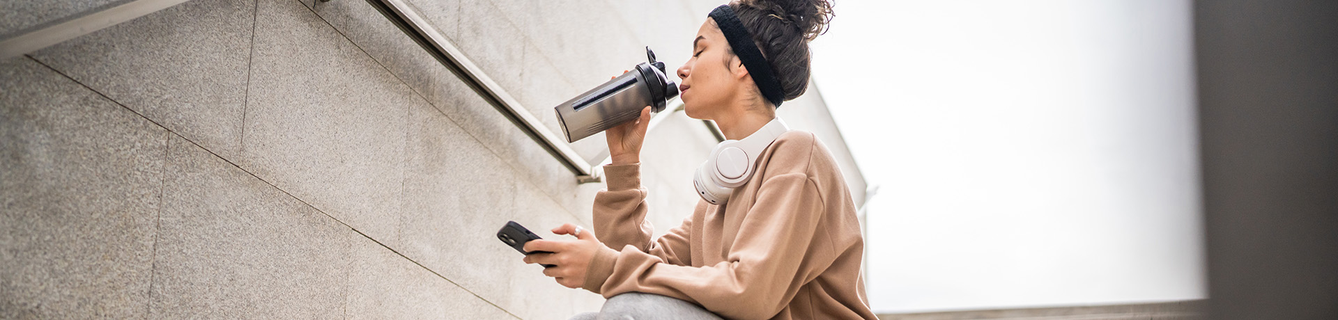 Frau sitzt auf Treppe und nimmt Schluck aus einem Shaker