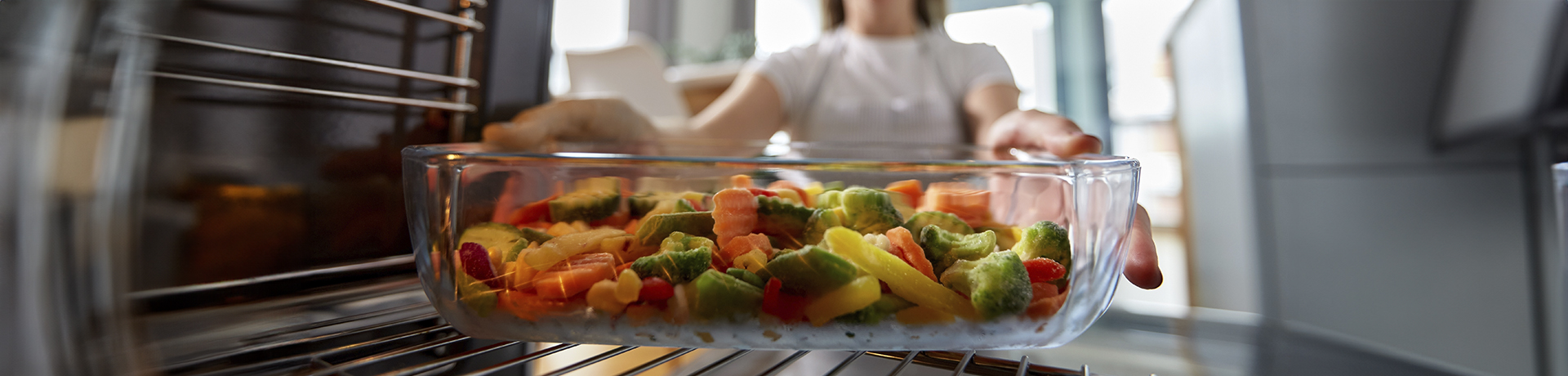 Junge Frau schiebt Ofengemüse in den Backofen