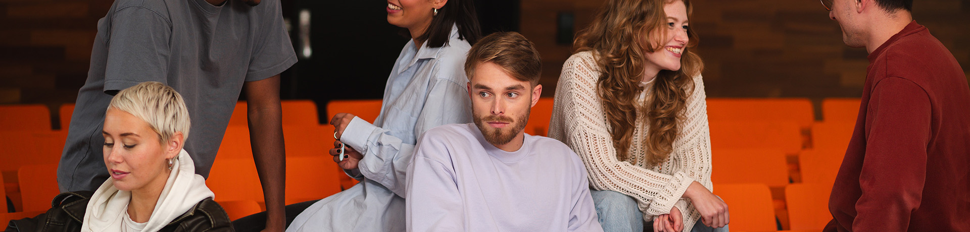 Junger Student sitzt in einer Gruppe von Menschen und schaut abwesend