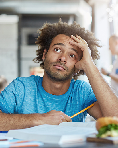 Junger Mann hat Kopf in die Hand gestützt und schaut nachdenklich nach oben