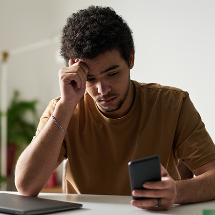 Ein junger Mann schaut unglücklich auf sein Handy. 
