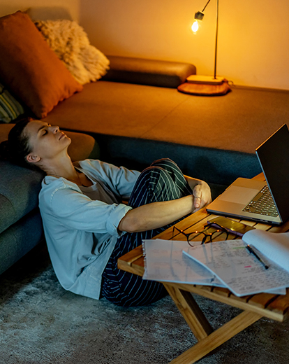 Frau sitzt zusammengekauert auf dem Boden vor ihrem Laptop 