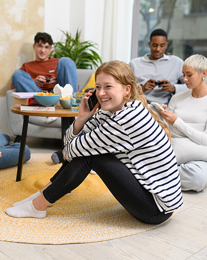 Junge Frau sitzt in einer Gruppe von Menschen und telefoniert lächelnd