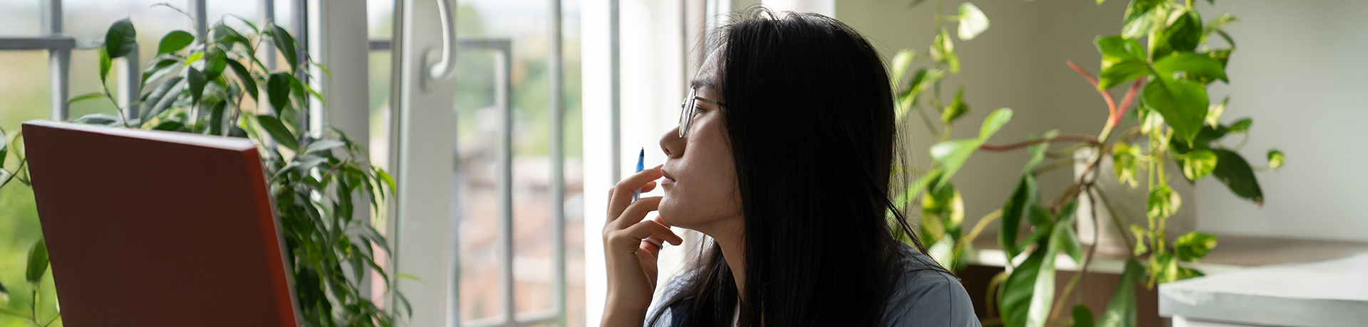Junge Frau an einem Schreibtisch blickt gedankenverloren aus dem Fenster
