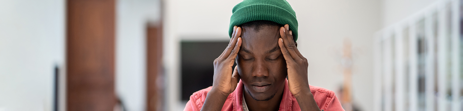 Junger Mann sitzt mit Kopf in die Hände gestützt an einem Tisch