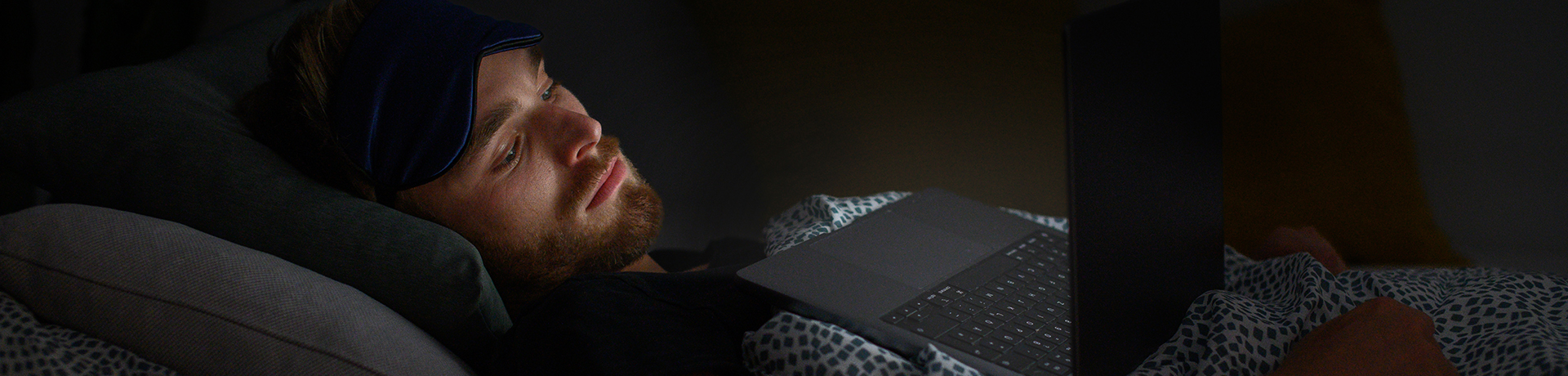 Junger Mann liegt im Bett und schaut auf seinen Laptop