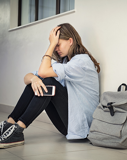 Studentin sitzt resigniert an einer Wand und stützt den Kopf in eine Hand