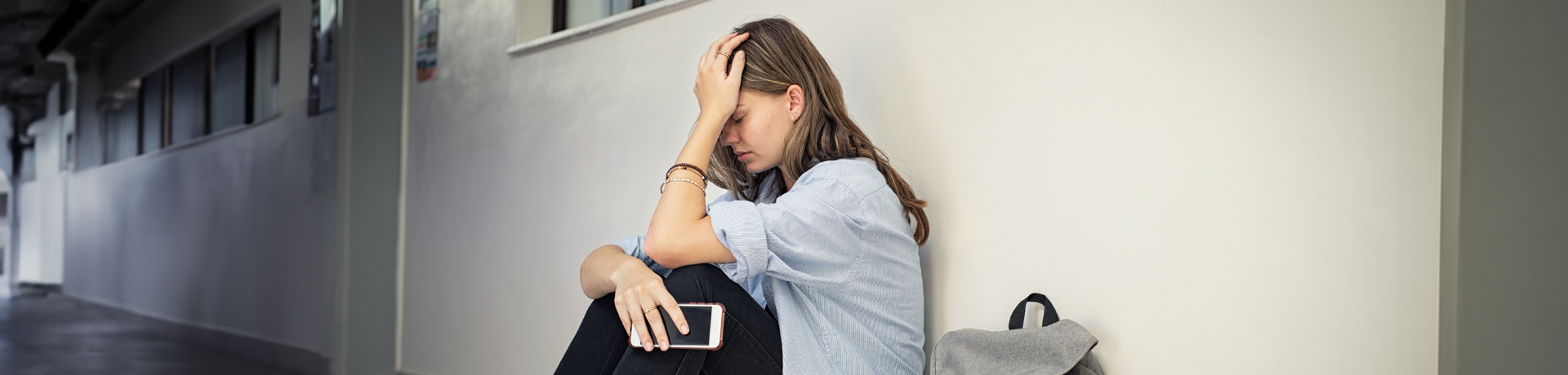 Studentin sitzt resigniert an einer Wand und stützt den Kopf in eine Hand