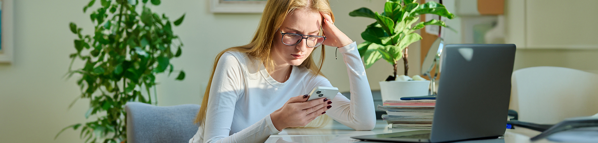 Junge Frau stützt Kopf in die Hände und schaut nachdenklich in ihr Telefon
