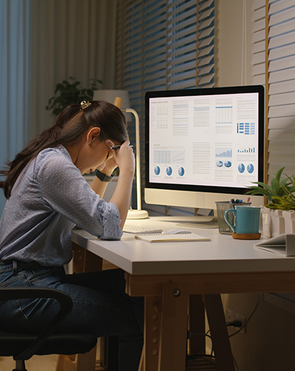 Frau sitzt vor ihrem Laptop am Schreibtisch und stützt Gesicht in ihre Hände