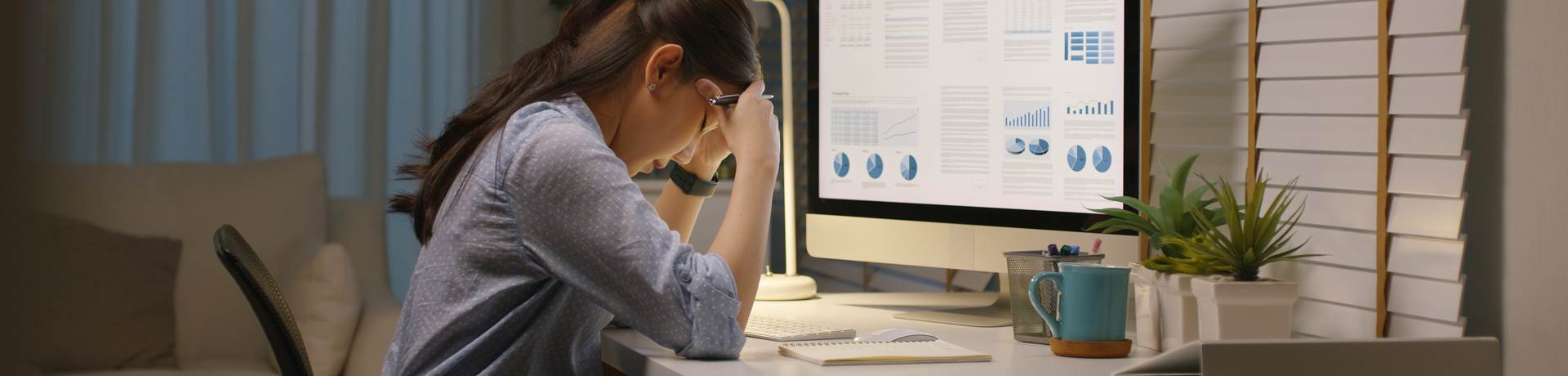 Frau sitzt vor ihrem Laptop am Schreibtisch und stützt Gesicht in ihre Hände