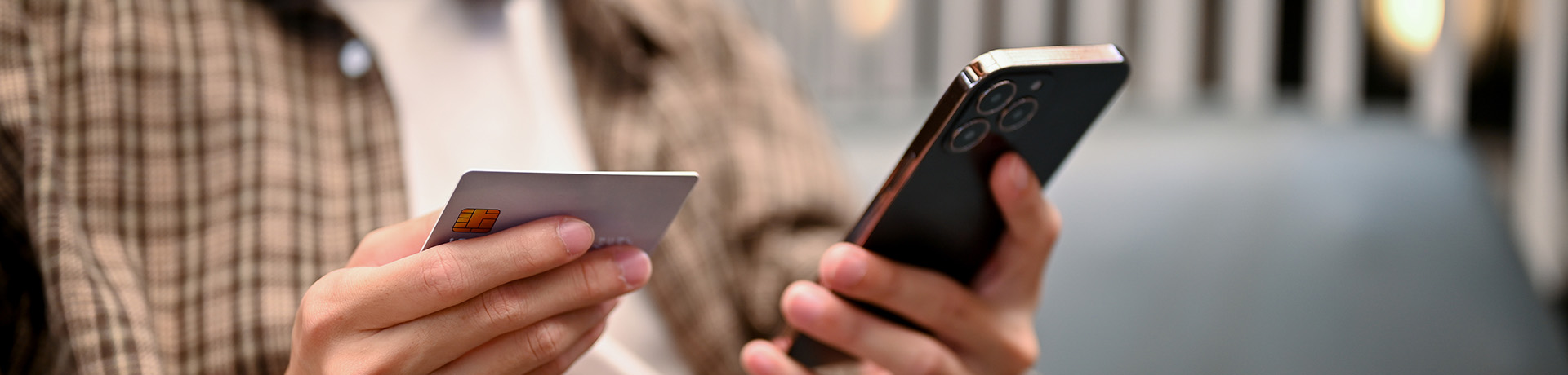 Person hält Kreditkarte in der einen und Handy in der anderen Hand