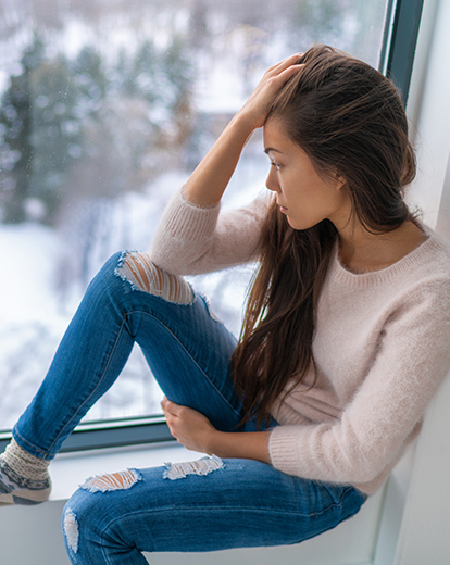 Junge Frau hat ihren Kopf in eine Hand gestützt und schaut deprimiert aus dem Fenster