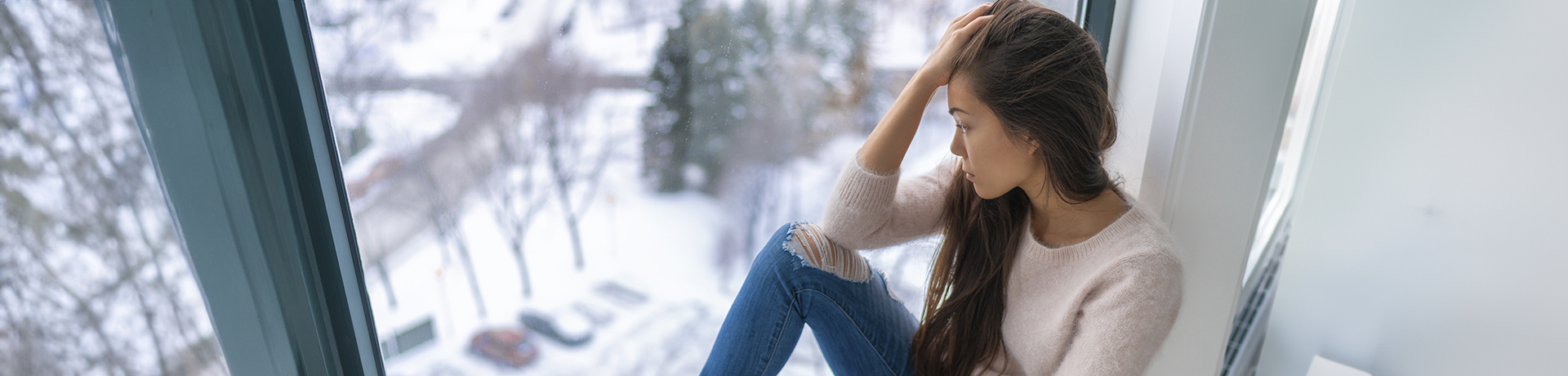 Junge Frau hat ihren Kopf in eine Hand gestützt und schaut deprimiert aus dem Fenster
