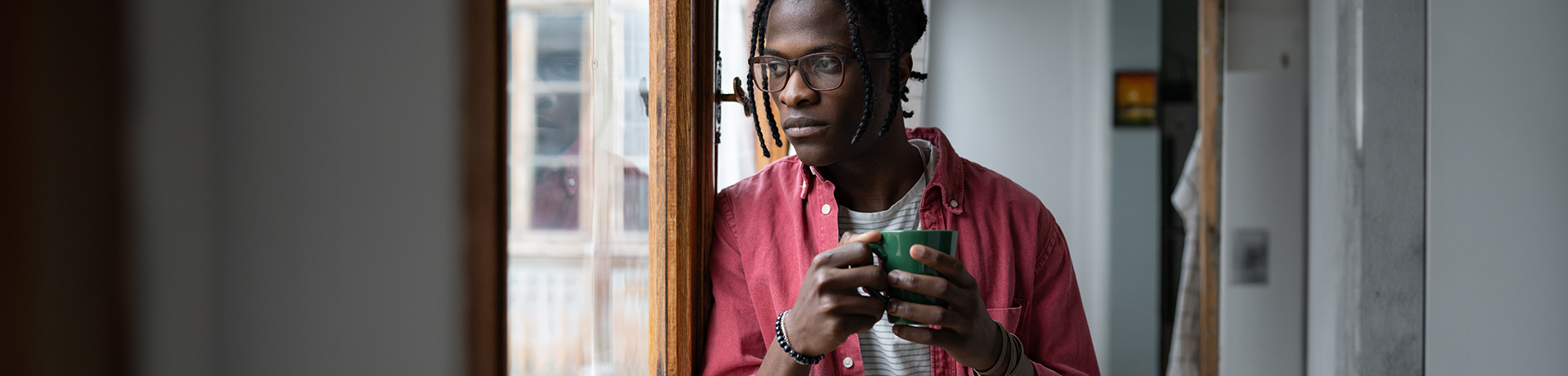Mann mit Tasse in der Hand schaut nachdenklich aus dem Fenster