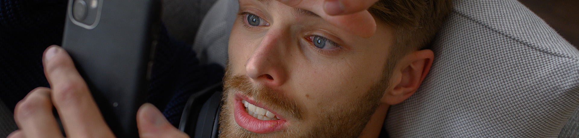 Mann mit verzweifeltem Gesichtsausdruck liegt im Bett und schaut auf sein Handy