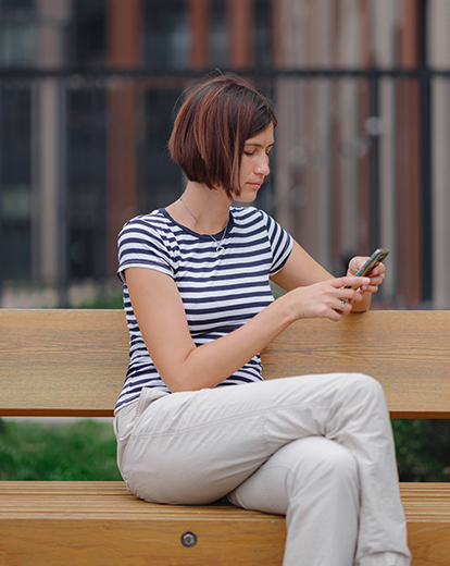 Frau sitzt auf einer Bank und schaut nachdenklich in ihr Smartphone