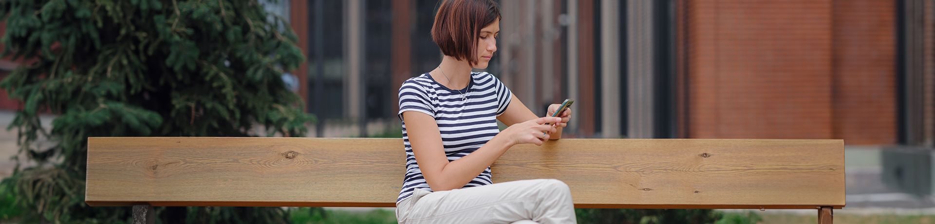 Frau sitzt auf einer Bank und schaut nachdenklich in ihr Smartphone