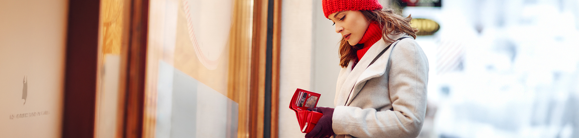 Frau im Winter schaut in ihr Portmonee vor einem Geschäft