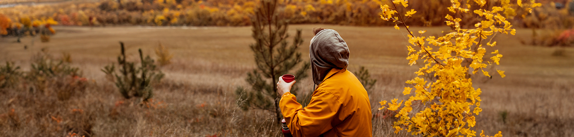 Mann sitzt mit Regenjacke und Tasse in der Natur