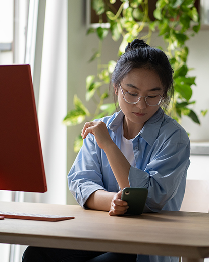 Frau vor Laptop schaut aufs Handy