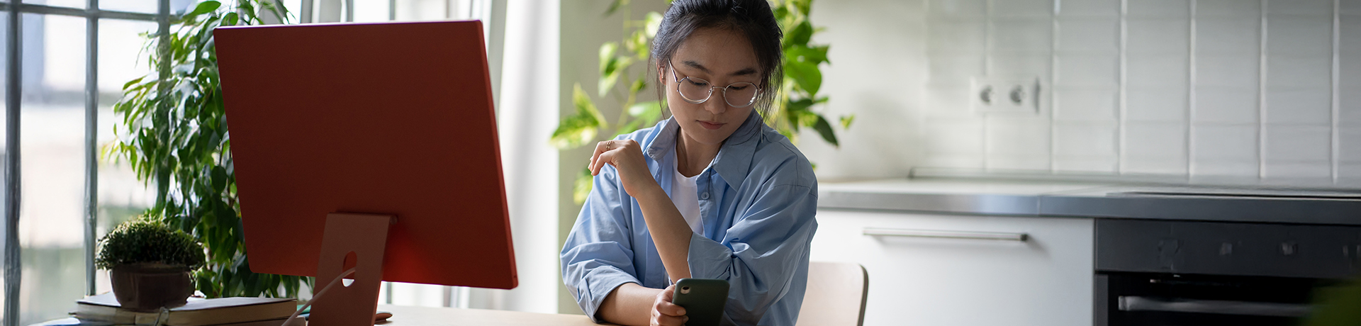 Frau vor Laptop schaut aufs Handy