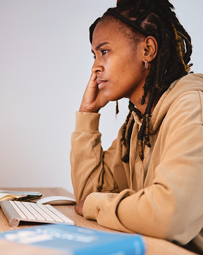 Junge Frau sitzt nachdenklich vor ihrem Laptop.