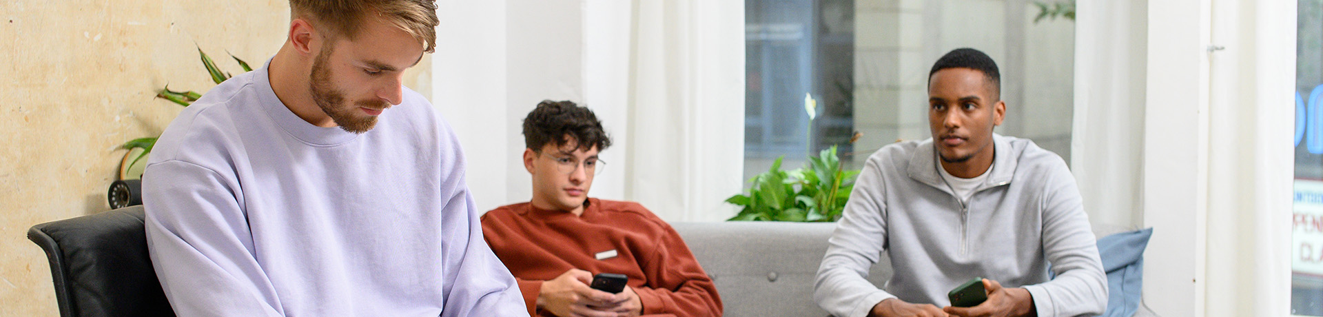 Drei junge Männer sitzen auf einer Couch und schauen in ihre Handys