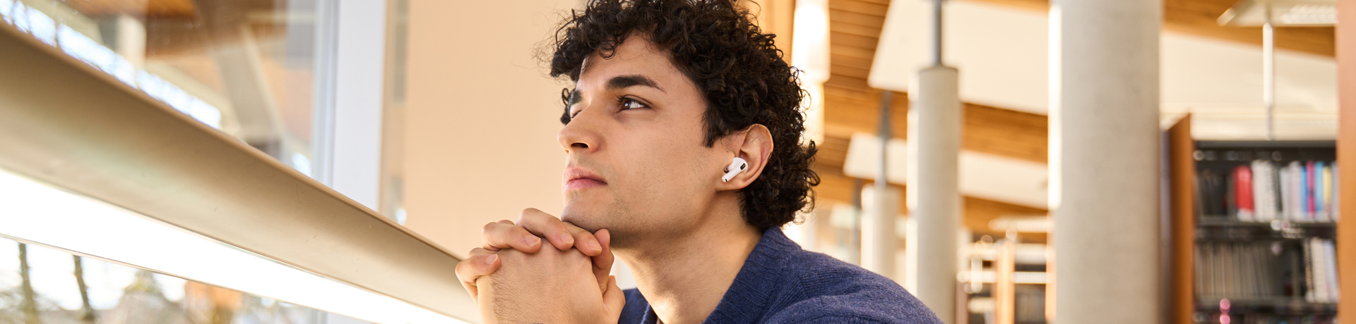 Junger Mann sitzt nachdenklich in der Bibliothek