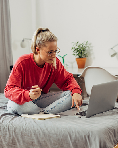 Junge Frau sitzt vor ihrem Laptop auf dem Bett