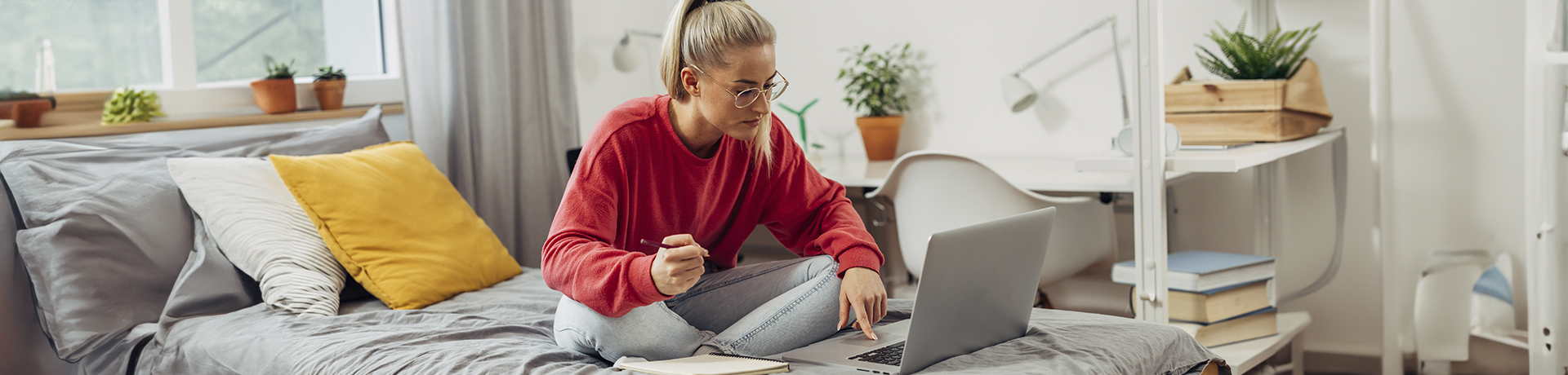 Junge Frau sitzt vor ihrem Laptop auf dem Bett