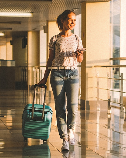Junge Frau lachend alleine am Flughafen mit Koffer