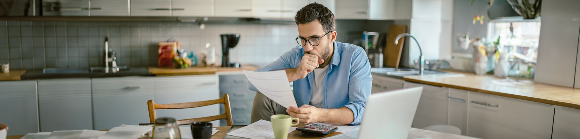 Mann sitzt in der Küche an einem Tisch vor Papieren