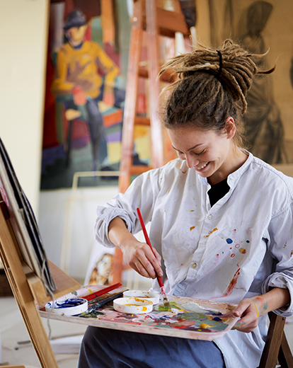 Junge Frau in einem Malerkittel steht vor einer Canvas und malt mit einem Pinsel