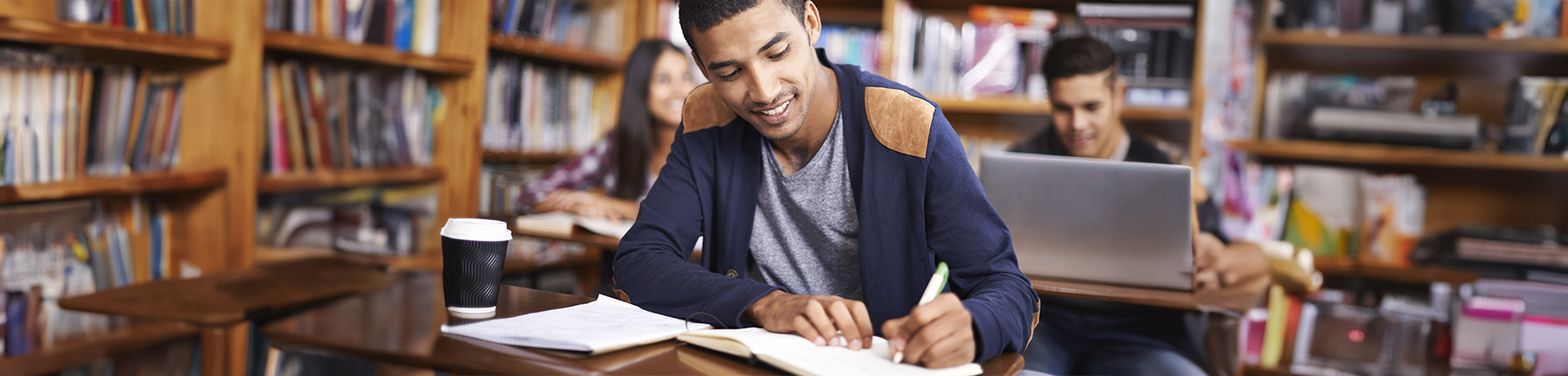 Junger Mann sitzt lachend im Unterricht und schreibt etwas auf Papier