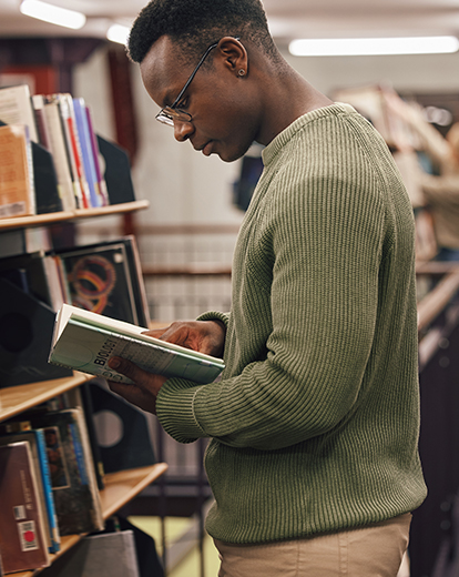 Student ist in Bibliothek über ein Buch gebeugt