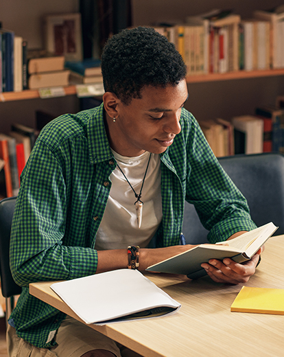 Student sitzt in Bibliothek über ein Buch gebeugt