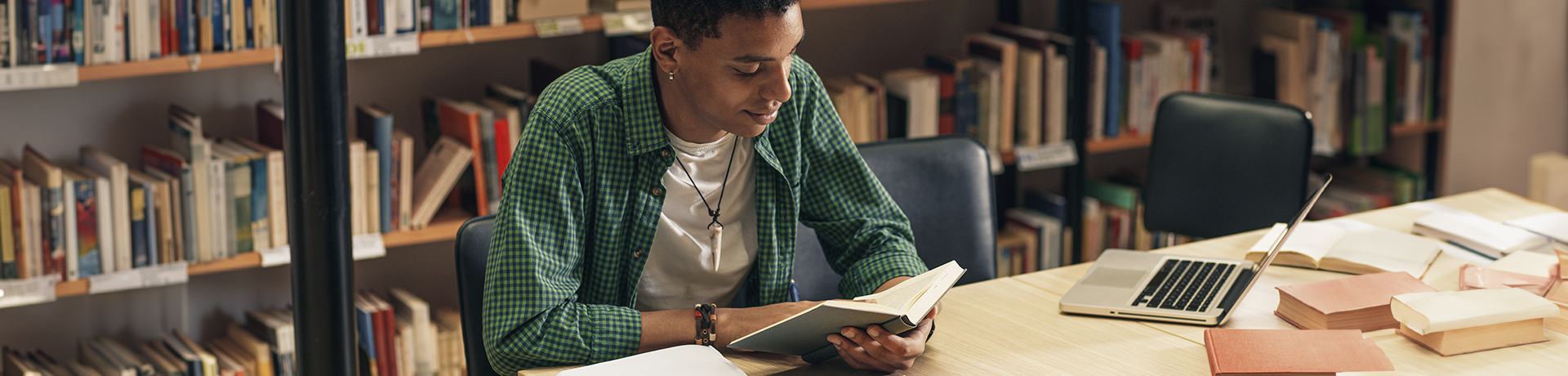 Student sitzt in Bibliothek über ein Buch gebeugt