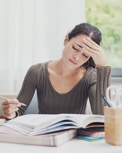 Junge Frau sitzt mit Kopf in die Hand gestützt vor einem Buch mit einem Stift in der Hand