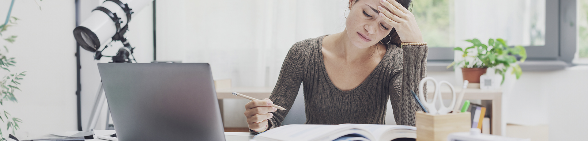 Junge Frau sitzt mit Kopf in die Hand gestützt vor einem Buch mit einem Stift in der Hand