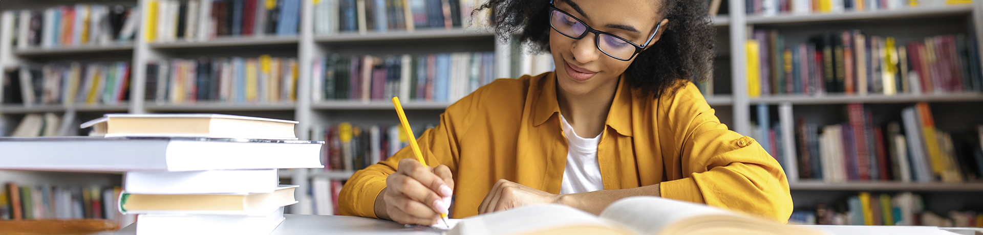 Frau sitzt in der Bibliothek vor einem Buch mit einem Stift in der Hand