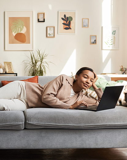 Frau liegt auf dem Sofa vor ihrem Laptop 